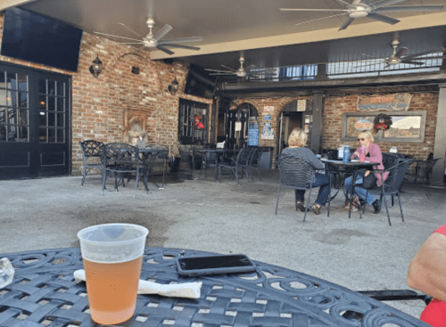 A casual outdoor seating area with tables, two women chatting, and a beer on the table in the foreground.