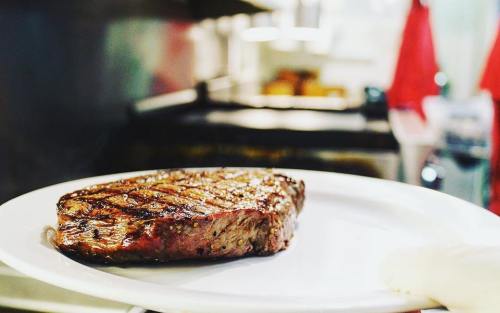 A perfectly grilled steak on a white plate, with grill marks and a smoky background.
