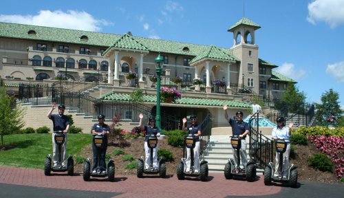 A group of six people on Segways in front of a large, elegant building with green roofs and colorful flowers.