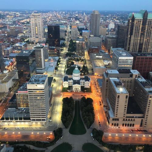 Aerial view of a city skyline at dusk, featuring a central dome building surrounded by illuminated streets and skyscrapers.