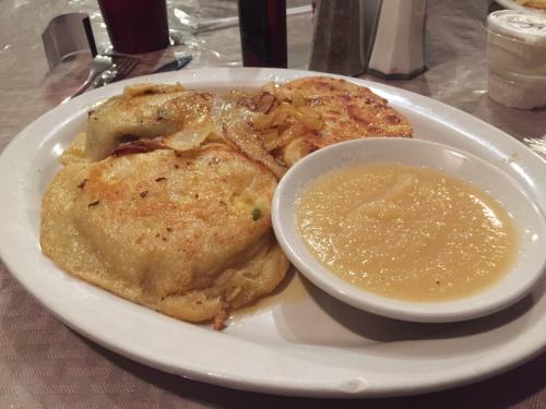 A plate of golden-brown fried dumplings with sautéed onions, served with a side of applesauce.