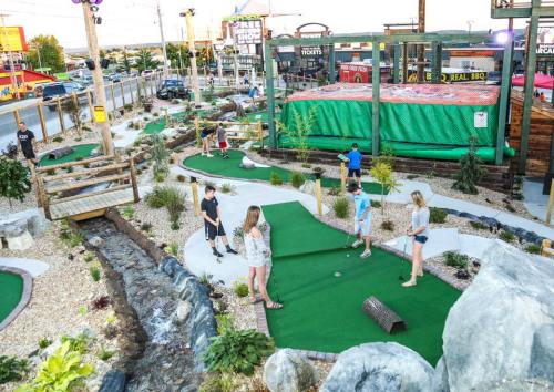 A mini-golf course with players, surrounded by rocks, plants, and a small stream, under a clear sky.