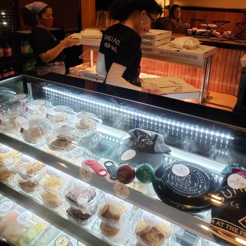 A dessert display case with various treats, two staff members preparing orders in a cozy shop setting.