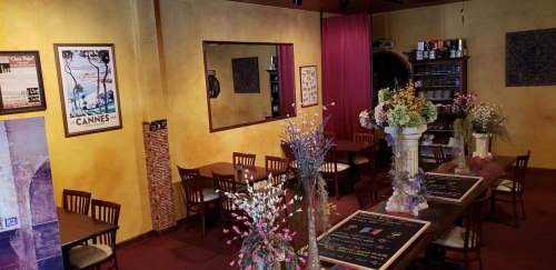 Cozy restaurant interior with yellow walls, wooden tables, and floral decorations, featuring mirrors and menu boards.