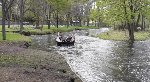 A group of people in a small boat on a calm river, surrounded by trees and greenery.