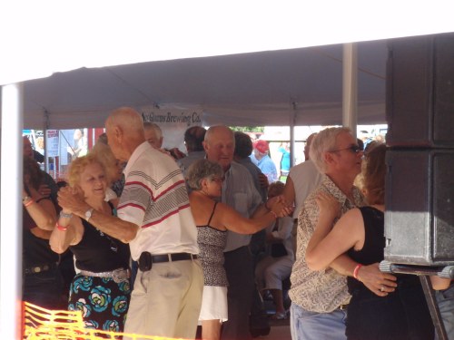 A lively gathering of older couples dancing under a tent at a festive event.