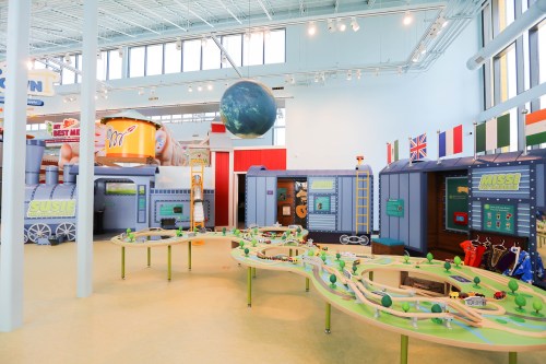A colorful indoor play area featuring a train track, interactive exhibits, and a large globe hanging from the ceiling.