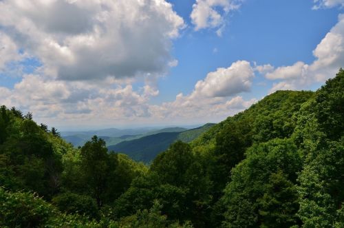 Lush green mountains under a bright blue sky with fluffy white clouds, showcasing a serene natural landscape.