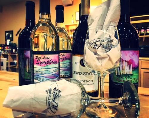 A collection of wine bottles and a wine glass with a logo, set on a wooden table in a cozy shop.