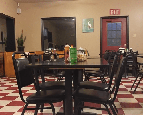 A cozy diner interior with checkered floors, empty tables, and condiments on a table. An exit door is visible.