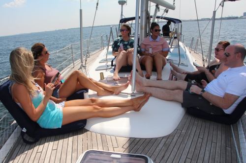 A group of six people relax on a sailboat, enjoying the sun and water, with some chatting and others on their phones.