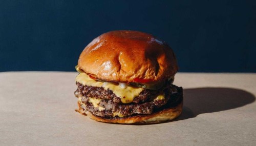A juicy cheeseburger with two beef patties, melted cheese, pickles, and a glossy bun on a neutral background.