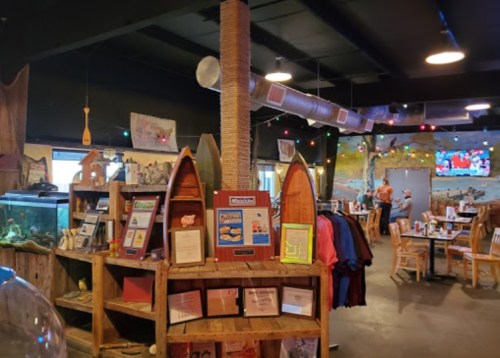 Interior of a cozy restaurant featuring wooden decor, colorful lights, and an aquarium, with tables and a mural in the background.