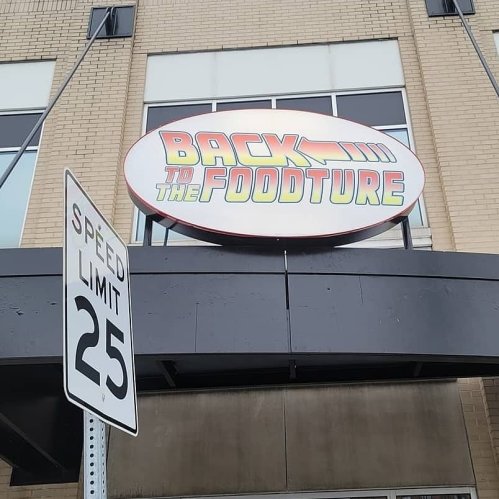 Sign for "Back to the Foodture" above a building, with a 25 mph speed limit sign in the foreground.