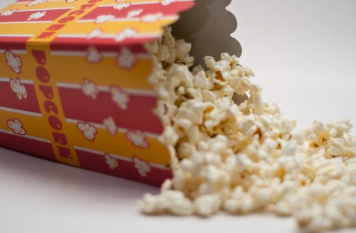 A colorful popcorn box tipped over, spilling fluffy popcorn onto a white surface.