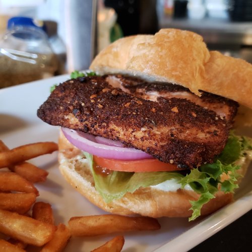 A crispy fish sandwich with lettuce, tomato, onion, and sauce, served with a side of golden fries.