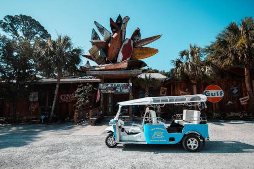 A blue tuk-tuk parked in front of a colorful, artistic building with palm trees and vintage signs.