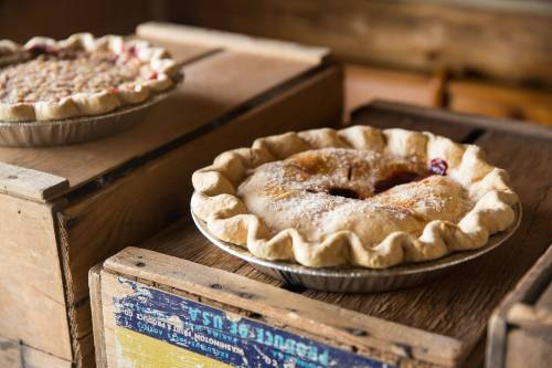 Two freshly baked pies on wooden crates, one with a lattice top and the other with a smooth crust, both dusted with sugar.
