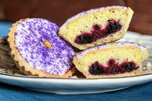 A plate of colorful pastries with a purple icing topping and a berry filling, showcasing a cross-section of one.
