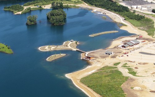 Aerial view of a lake with small islands, sandy shores, and a developing recreational area.