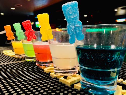 Colorful shots lined up on a bar, each topped with a gummy bear in various colors.