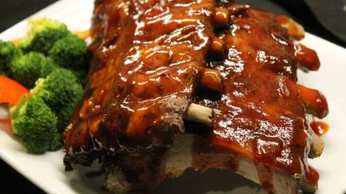 A plate of glazed barbecue ribs served with broccoli and red bell pepper on the side.