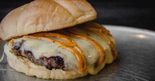 A close-up of a cheeseburger with melted cheese and a drizzle of sauce on a soft bun, served on a metal plate.