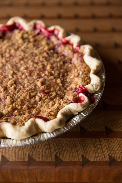 A freshly baked pie with a crumbly topping, resting in a silver pie dish on a wooden table.