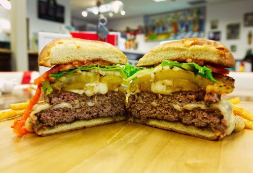 A juicy burger cut in half, layered with lettuce, tomato, pickles, and melted cheese, served with fries on the side.