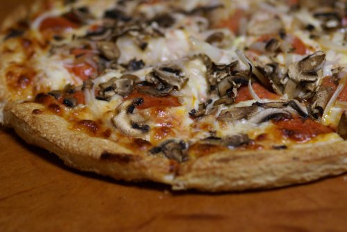A close-up of a pizza topped with mushrooms, tomatoes, and cheese on a golden crust, resting on a wooden surface.