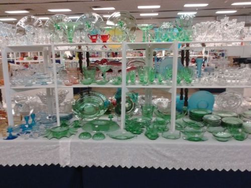 A display of various glassware, including green and clear pieces, arranged on white shelves at a market.