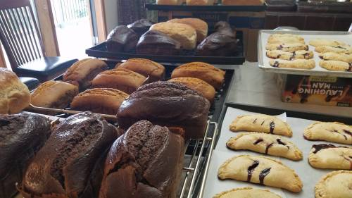 A variety of baked goods, including loaves of bread and pastries with fruit filling, cooling on wire racks.