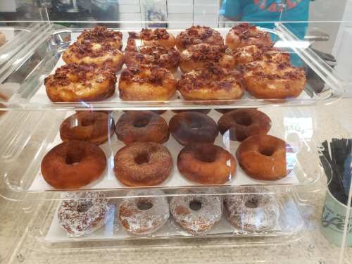 A display case with three tiers of assorted donuts, including glazed, chocolate, and cinnamon sugar varieties.
