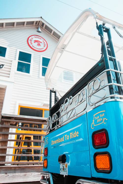 A blue tuk-tuk parked outside a building with a red logo, featuring a sign that says "Download To Ride."