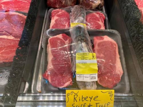 Display of ribeye steaks in a butcher shop, with a price tag and a sign reading "Ribeye Stuff & Truff."
