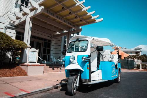 A blue and white tuk-tuk parked outside a building with a sign that reads "fish out of water." Clear blue sky above.