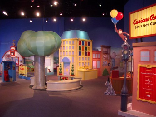 Colorful indoor play area featuring a large tree, buildings, and playful decorations, designed for children's exploration.