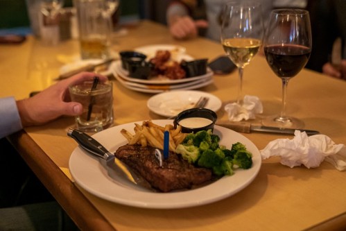 A plate with steak, fries, and broccoli, accompanied by drinks and napkins on a restaurant table.