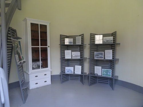 A small exhibit room with gray display panels and a white cabinet, featuring informational posters and photographs.