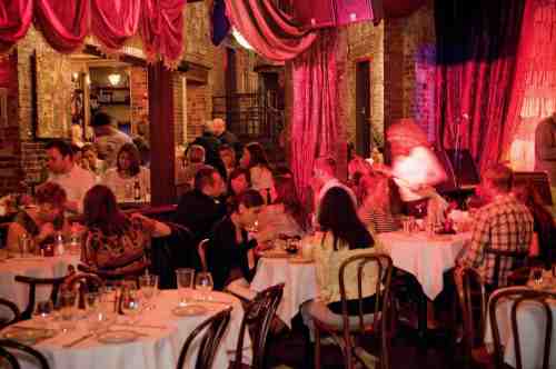 A lively restaurant scene with diners at tables, warm lighting, and a stage in the background.