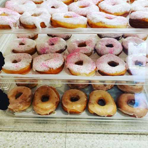 A display of assorted donuts, including glazed and frosted with pink sprinkles, stacked in clear containers.