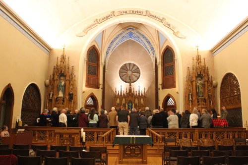 A group of people gathered in a church, facing an altar adorned with religious statues and intricate woodwork.
