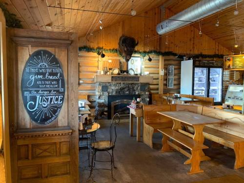 Cozy wooden interior of a café with a stone fireplace, rustic tables, and a chalkboard sign about justice.