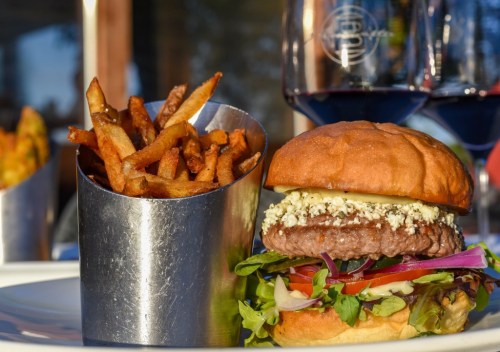 A juicy burger with lettuce, tomato, and cheese, served with a side of crispy fries in a metal cup.