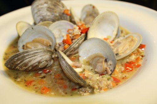 A bowl of clam chowder with clams, diced red peppers, and herbs in a creamy broth.