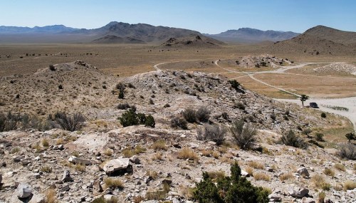 A vast, arid landscape with rocky hills and sparse vegetation under a clear blue sky.