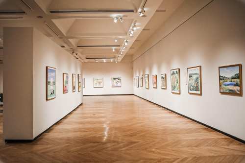 A spacious art gallery with framed paintings on the walls and polished wooden flooring.