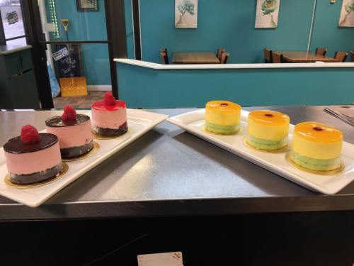 Two plates of colorful desserts: pink and green mousse cakes topped with raspberries and yellow jelly.