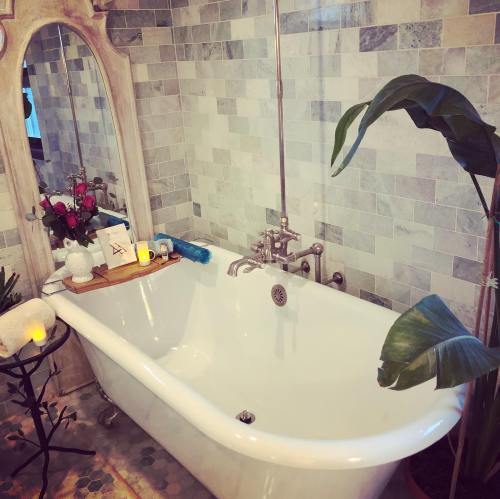 A cozy bathroom featuring a vintage bathtub, plants, candles, and a decorative mirror against a tiled wall.
