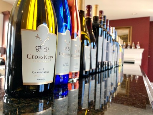 A row of colorful wine bottles from CrossKeys Vineyard on a dark countertop, with a cozy interior in the background.